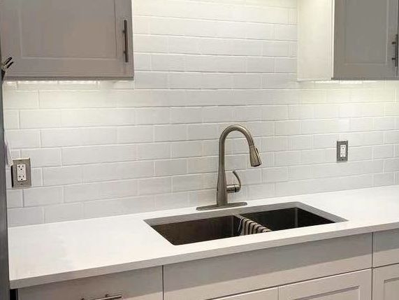 Kitchen with white cabinets, subway tile backsplash, and countertop. Stainless steel sink and faucet.