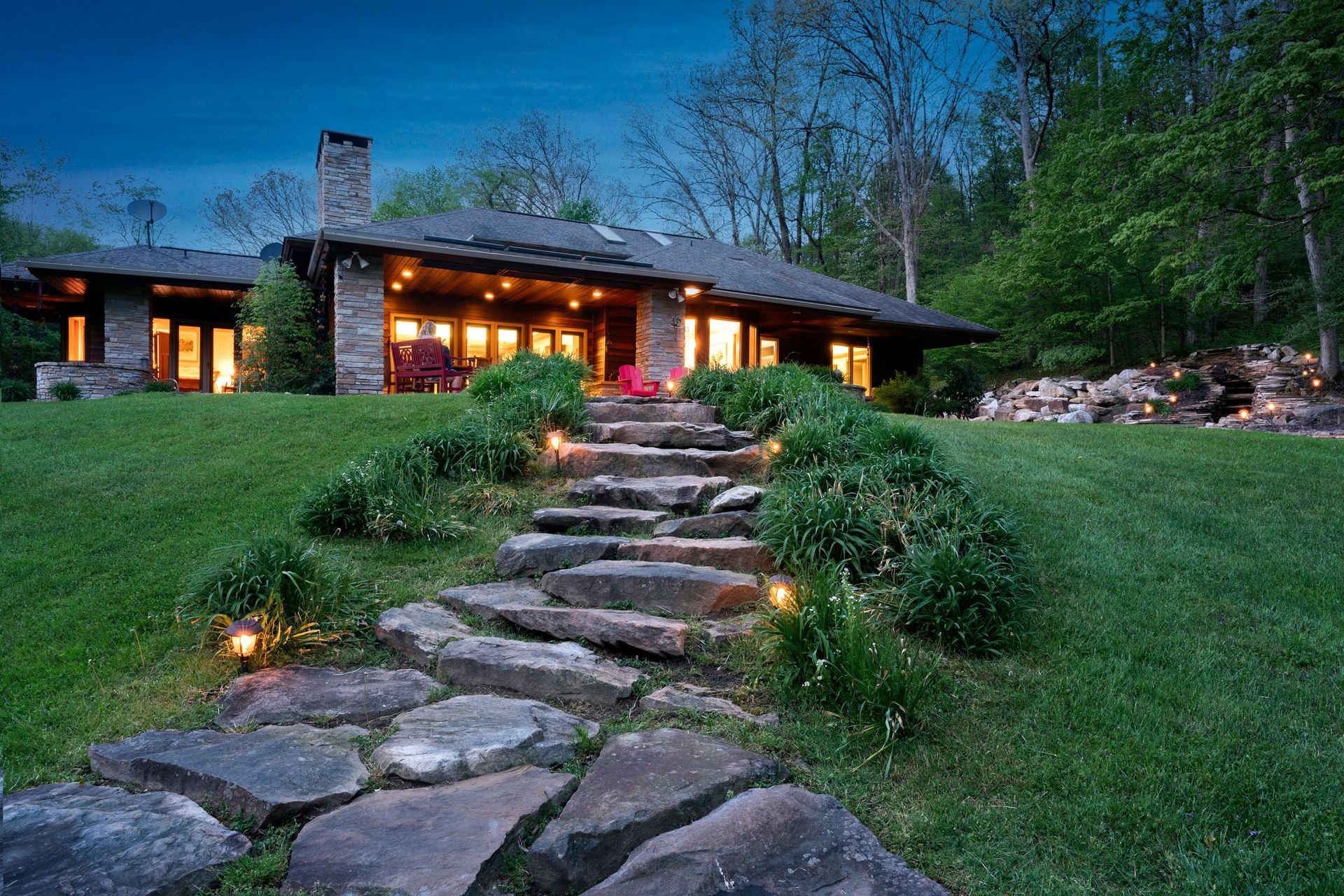 Outdoor garden pathway lights illuminating landscaped yard with shrubs and green lawn at dusk.