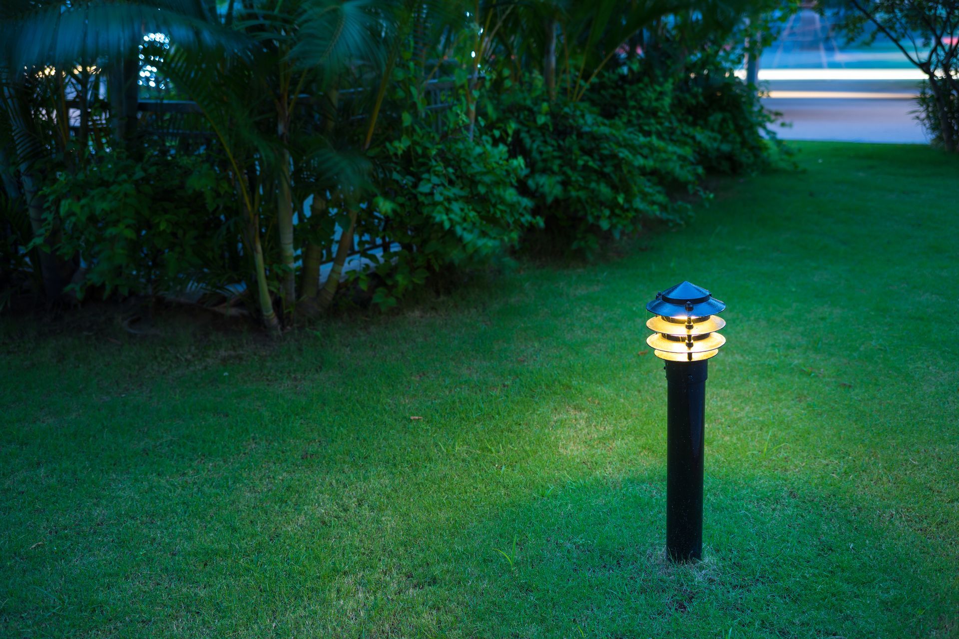 A single outdoor light illuminates a part of a garden, with grass and trees.