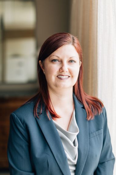 A woman in a suit is sitting in front of a window and smiling.