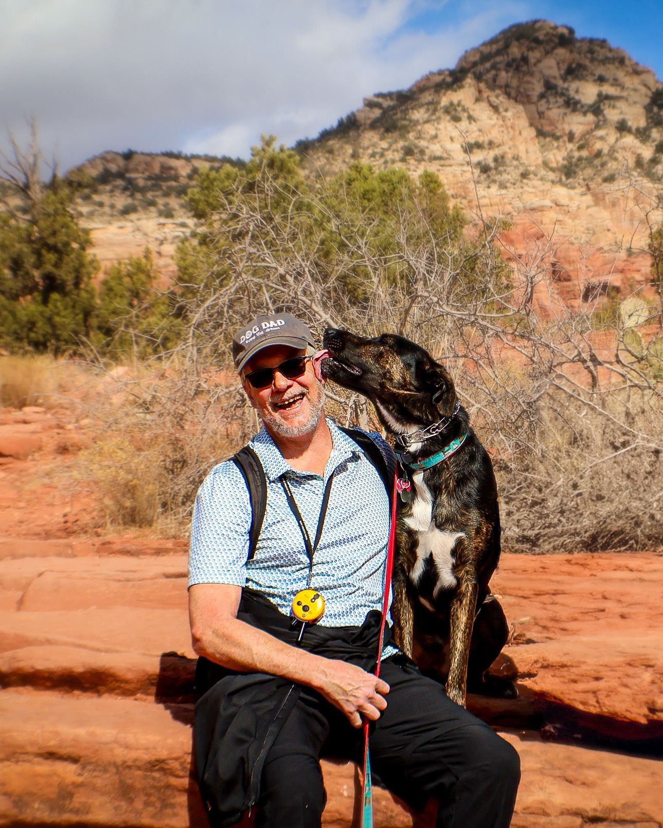 A man is sitting on a rock with a dog licking his face.