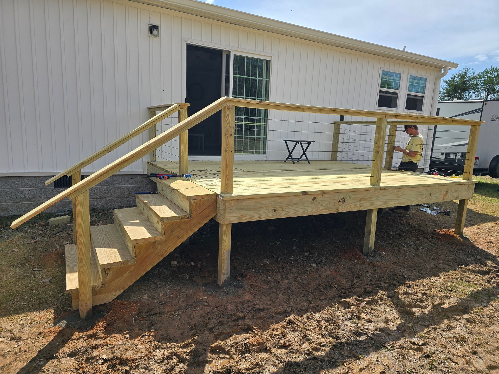 Wooden deck with steps and railing attached to a white building; a person is on the deck.