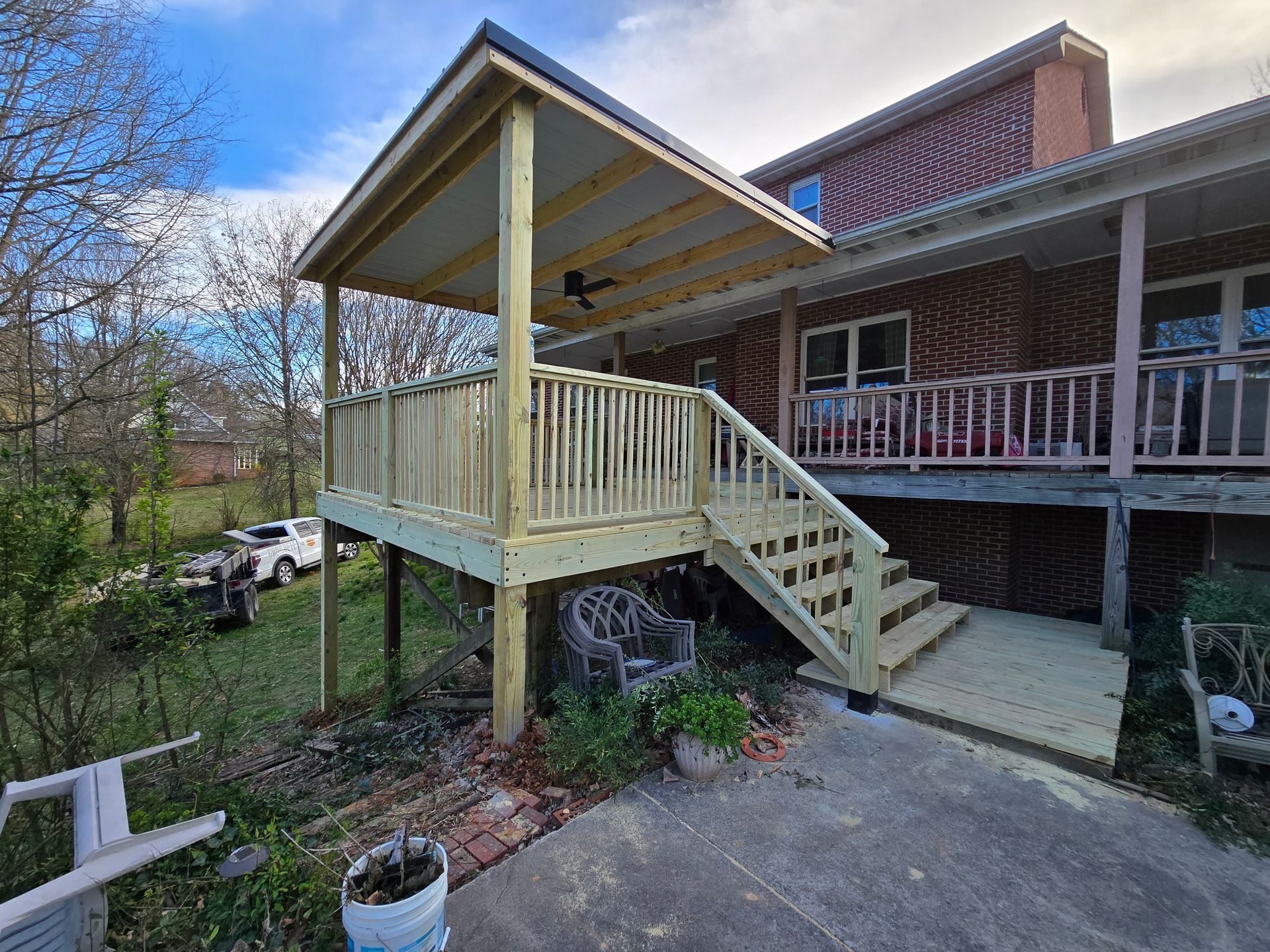 New wooden deck with covered porch, steps, and railing attached to a brick house.