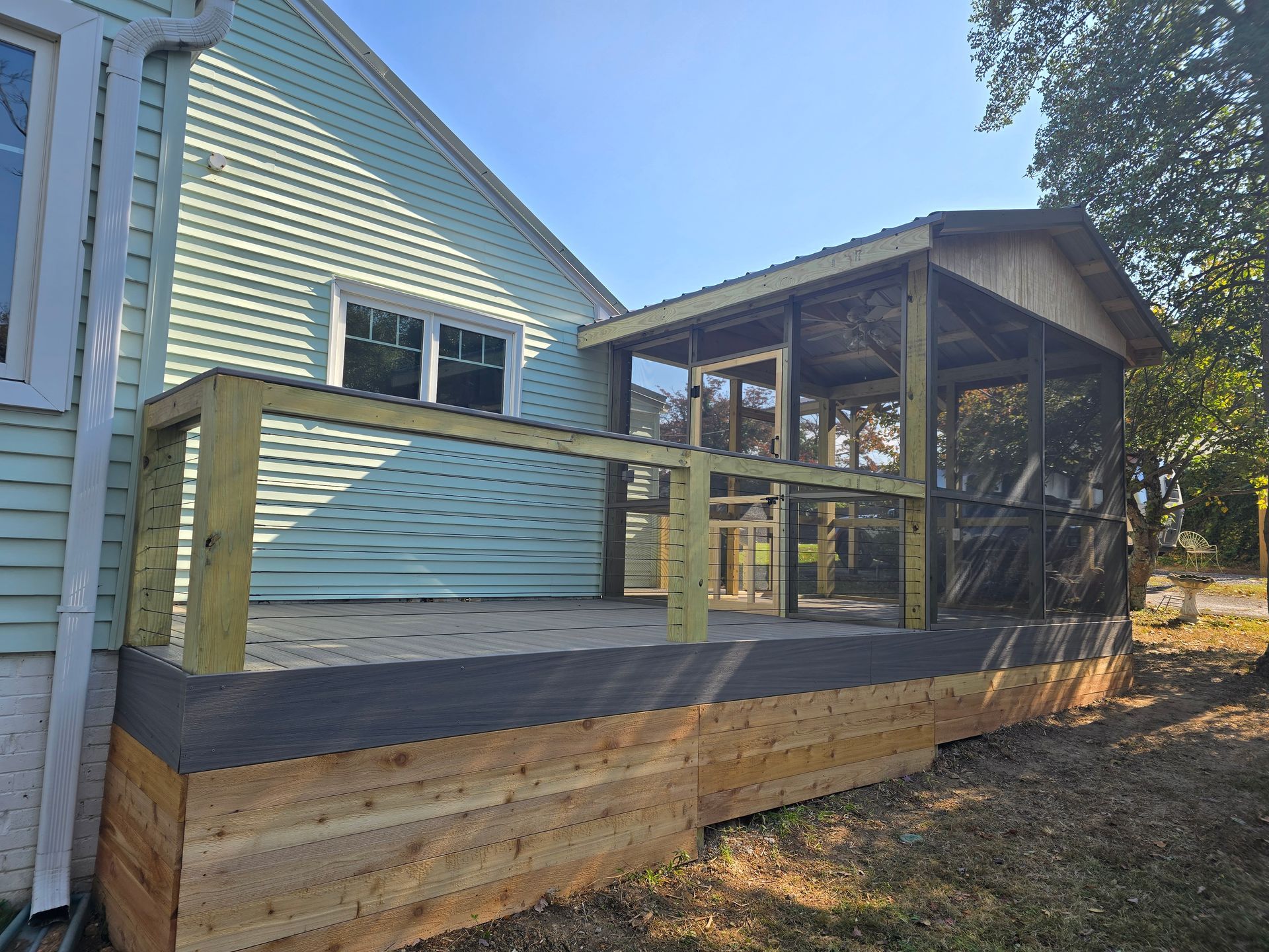 A newly built wooden deck with a screened-in porch attached to a light blue house.