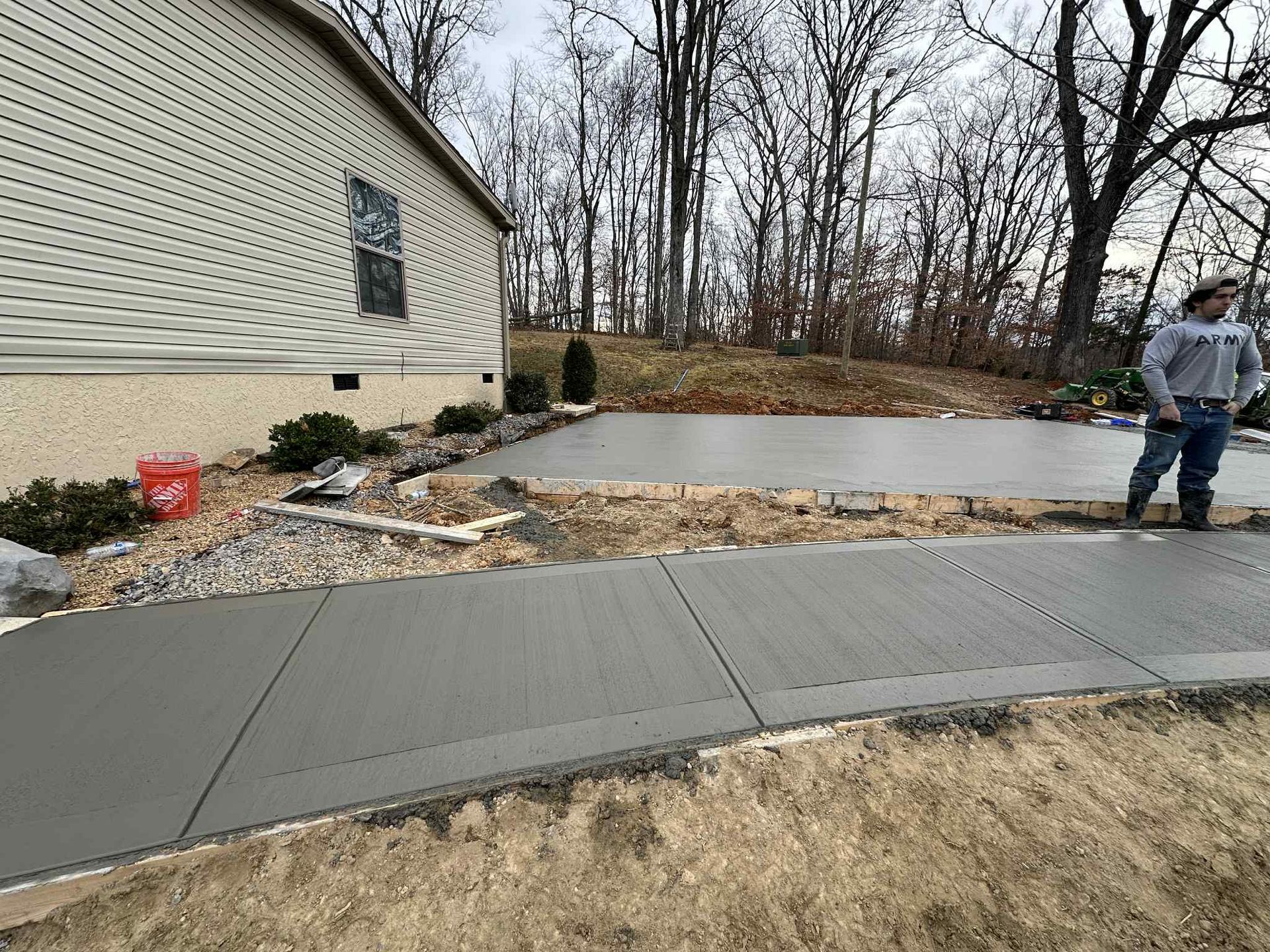 Freshly poured concrete driveway and sidewalk next to a house, person standing at the edge.