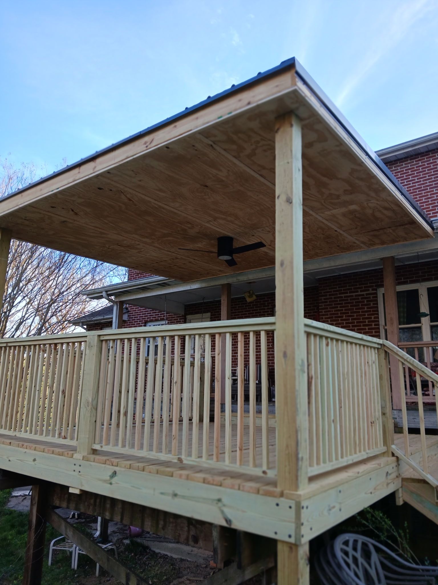 Wooden deck with a covered area and railing, attached to a brick building.