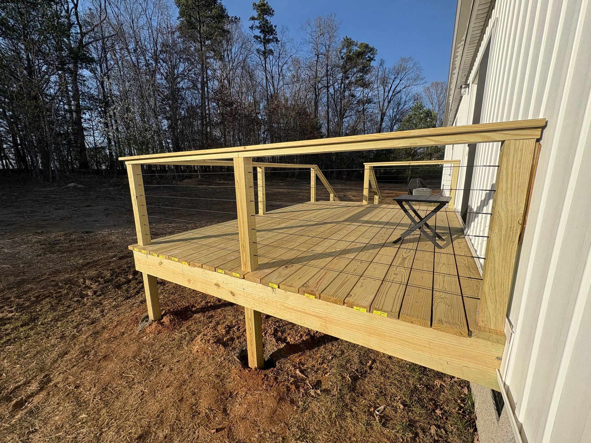 A newly constructed wooden deck with railings, attached to a house, on a sunny day.