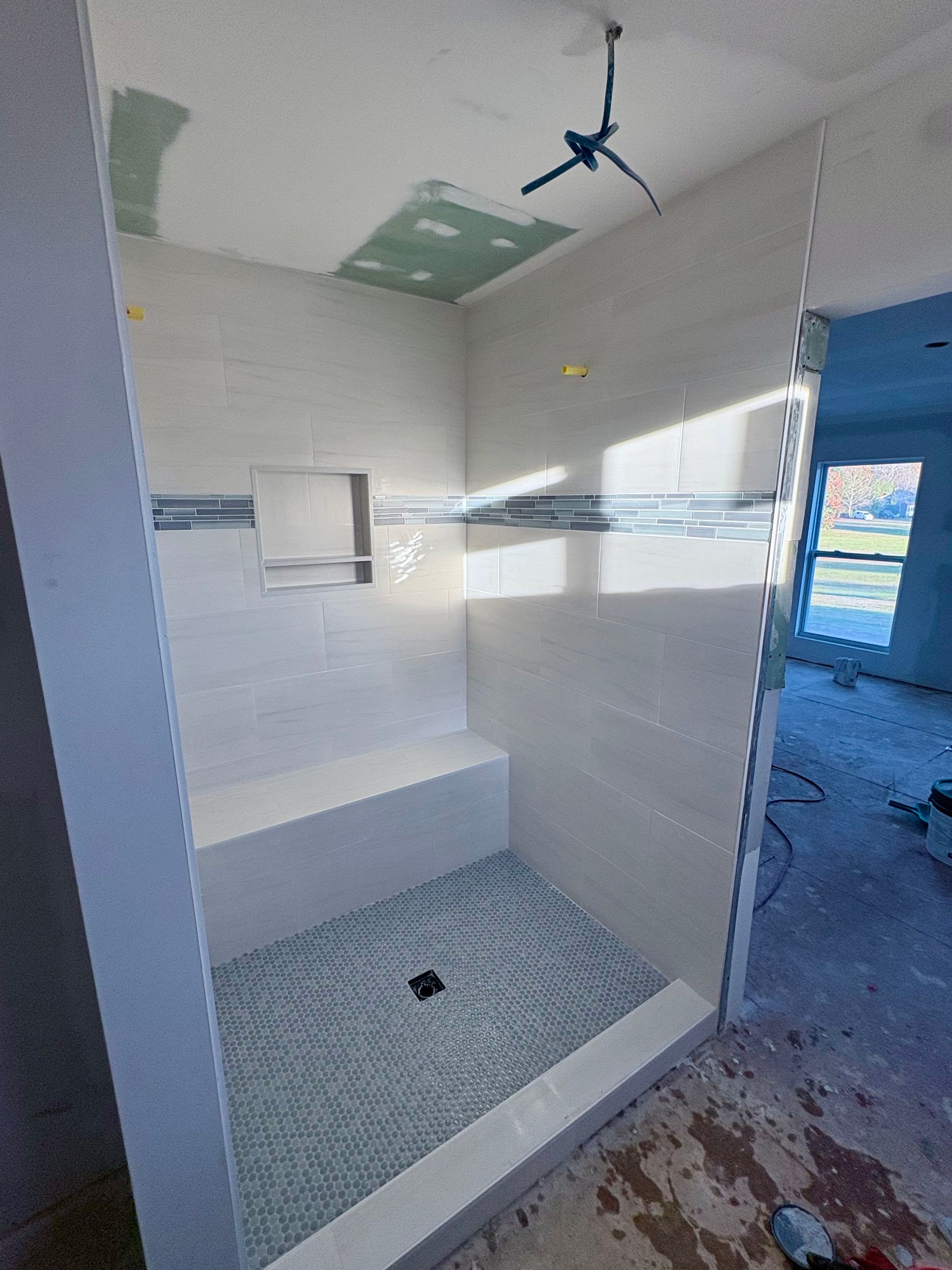 Newly tiled shower with built-in bench and niche; blue mosaic floor and accent tile.