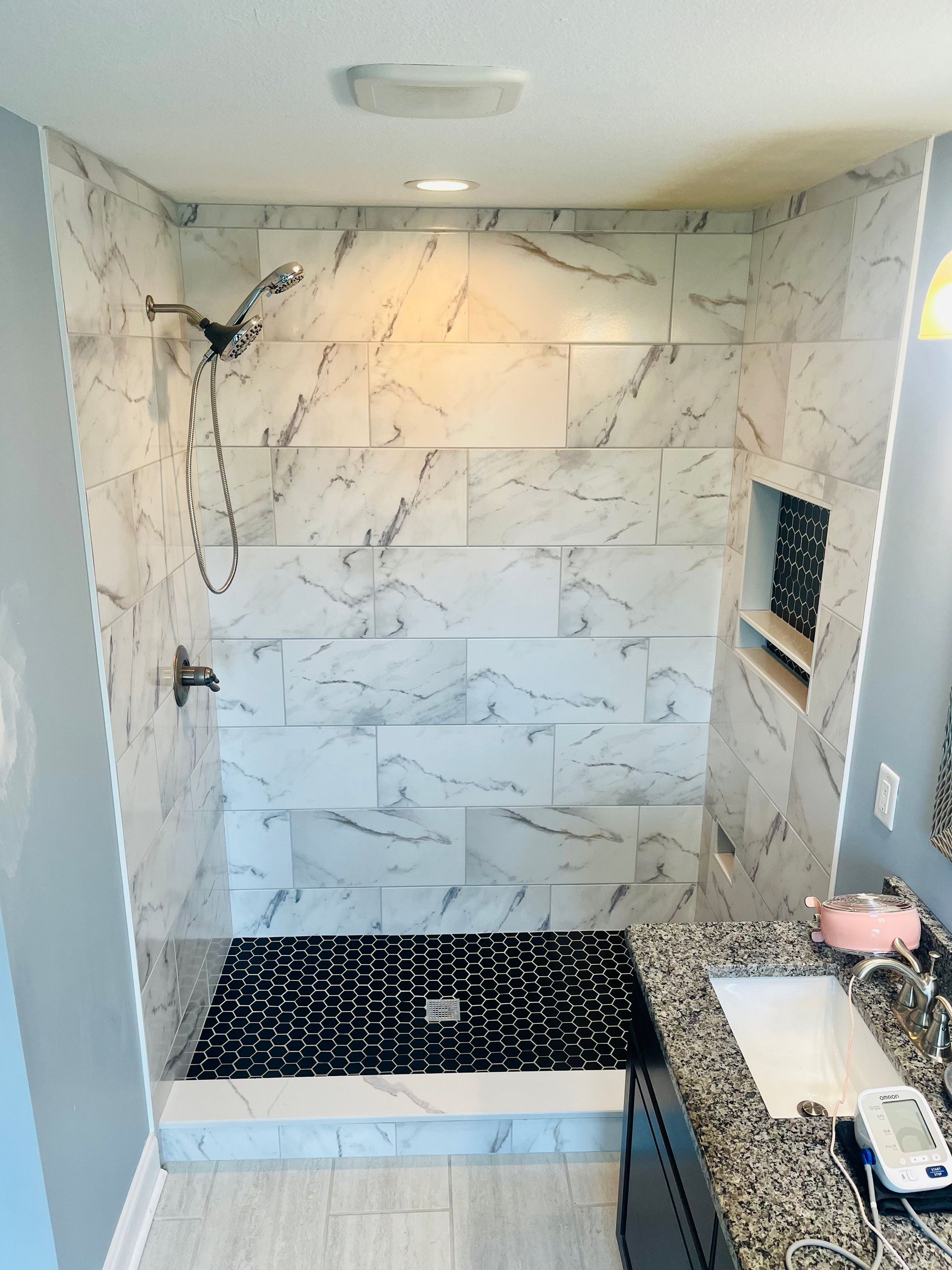 Newly tiled shower with black and white accent tiles and marble-look walls.