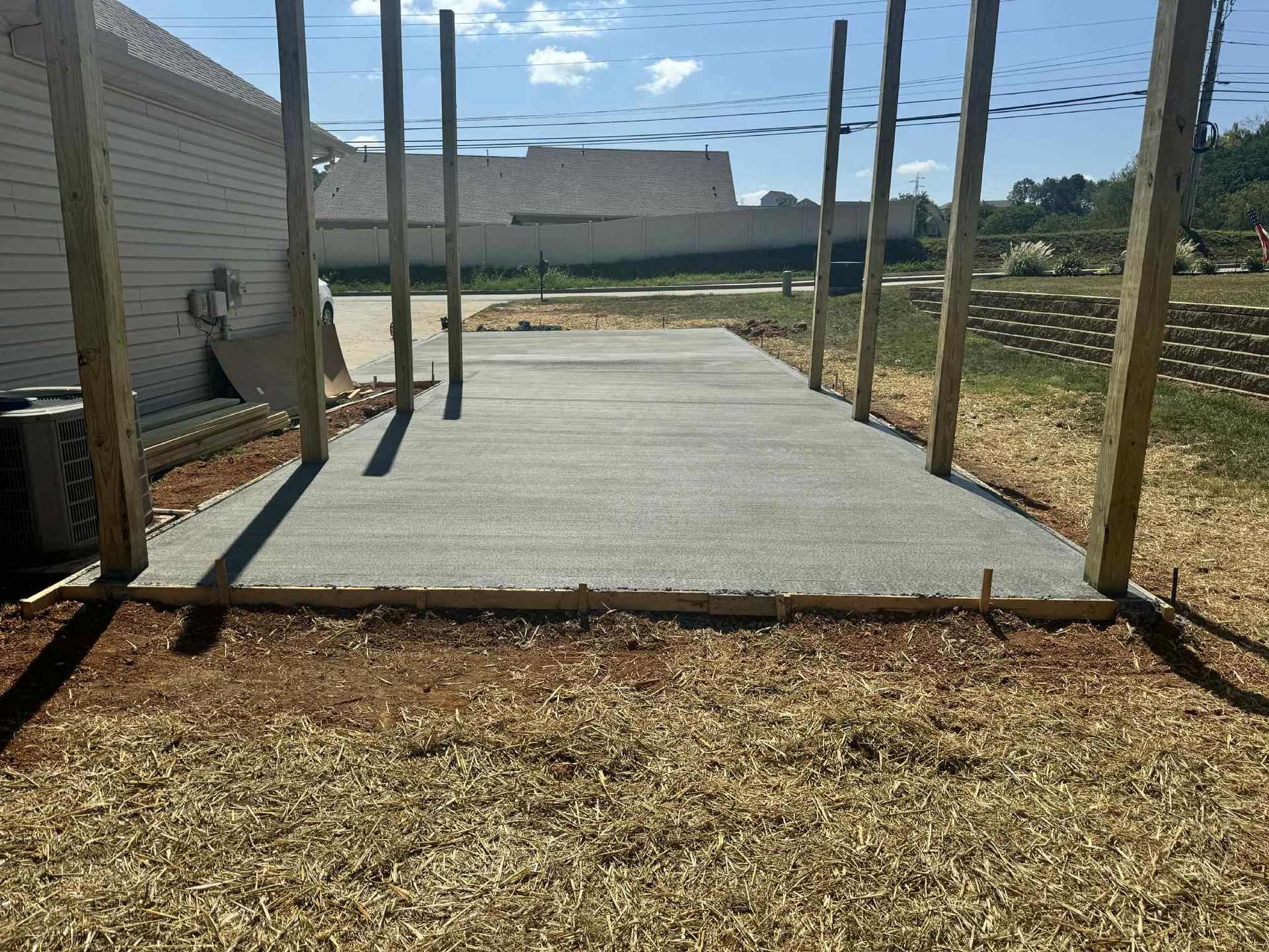 Concrete pad with wooden posts in a grassy yard, under a blue sky.