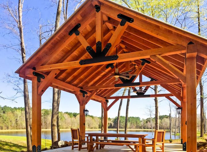 Wooden gazebo overlooking a lake, with table, chairs, and fans.