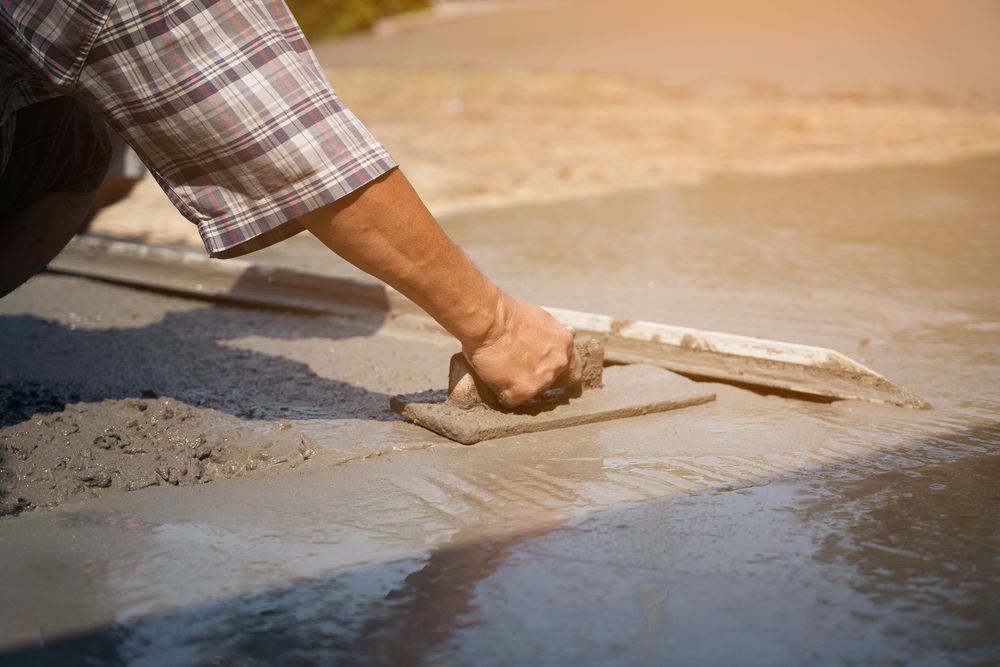 A man is spreading concrete on the ground with a trowel.