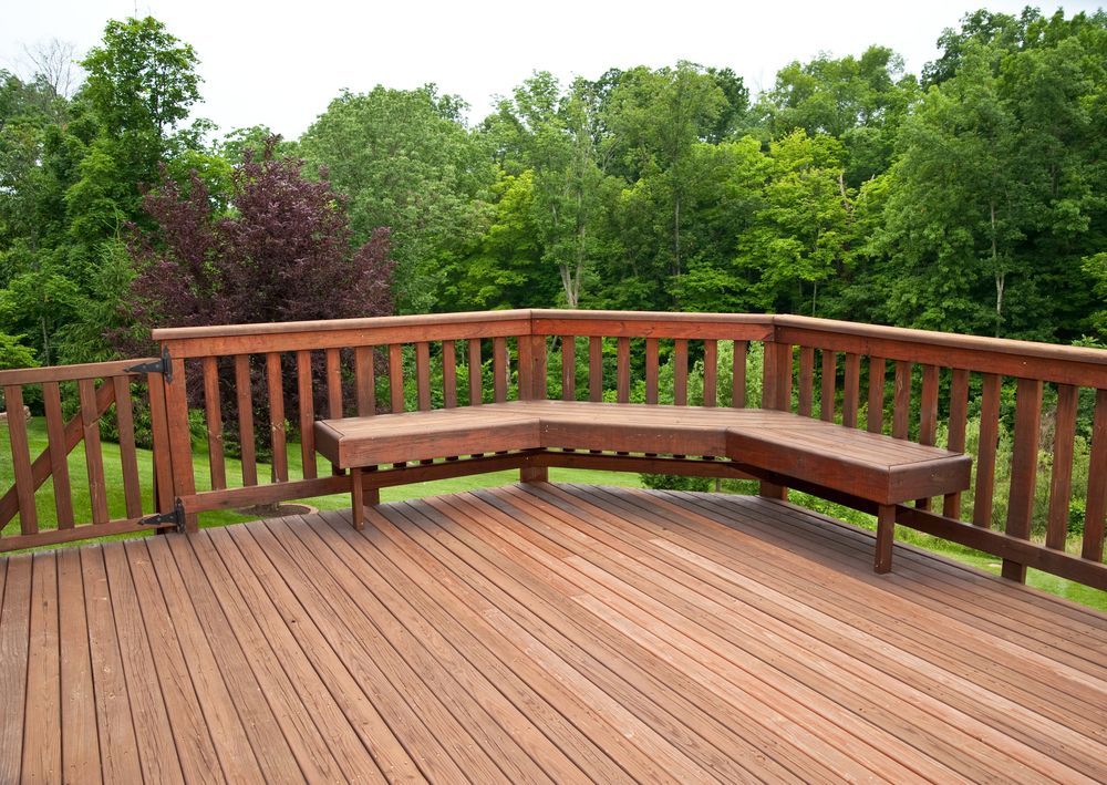 A wooden deck with a bench and trees in the background.