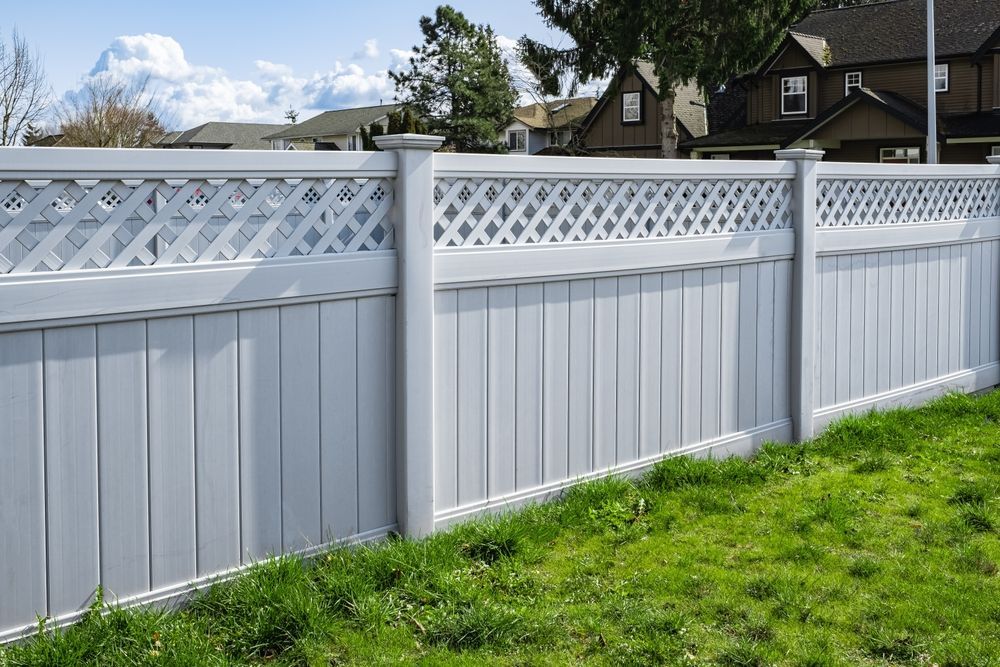 A white fence with a lattice design is surrounded by green grass.