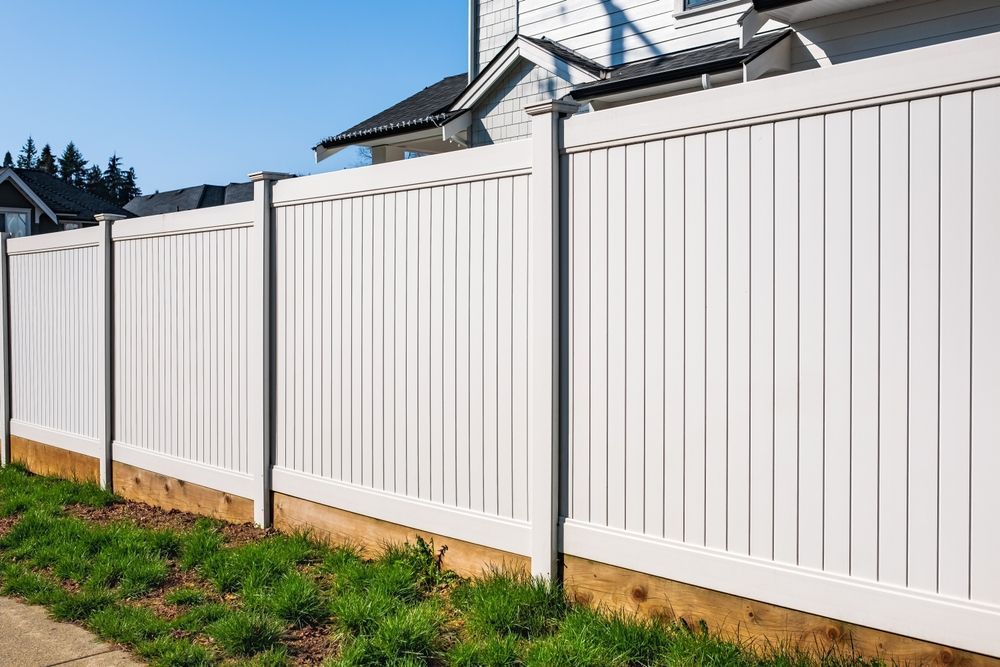 A white vinyl fence is surrounded by grass and a house.