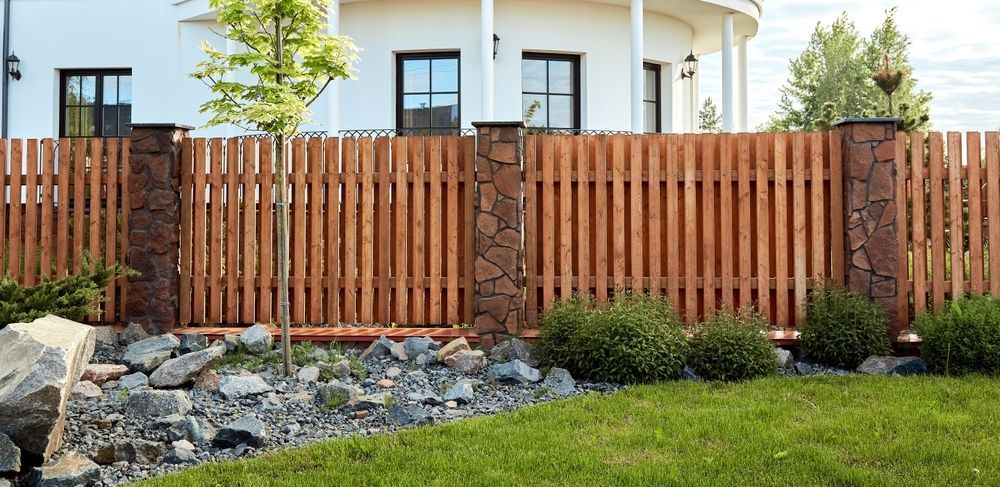 A wooden fence is in front of a large white house.