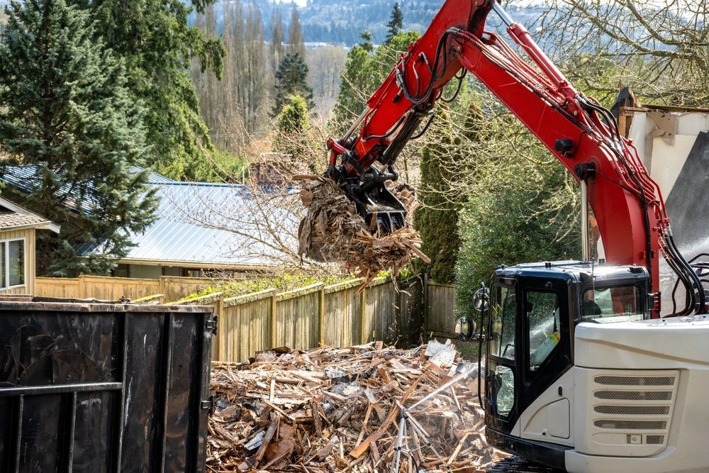 A red excavator is loading wood into a dumpster.