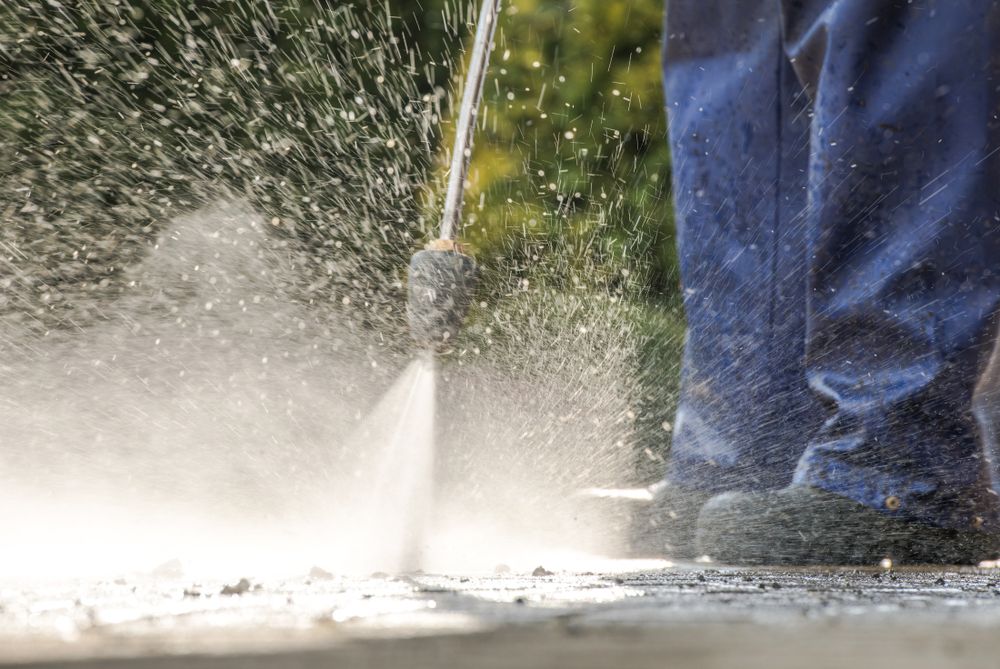 A person is using a high pressure washer to clean a sidewalk.