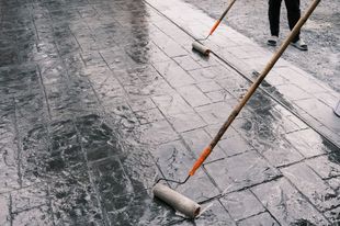 A person is painting a concrete floor with a roller.