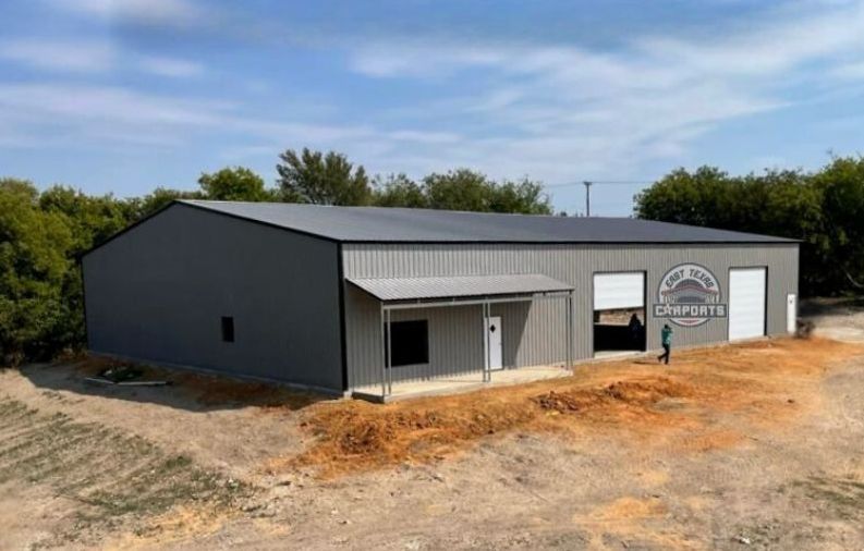 80'x100'x16' Vertical Panel Metal Commercial Garage.  Panels are silver with white roll up doors, a silver lean-to awning, a walk in door and windows.