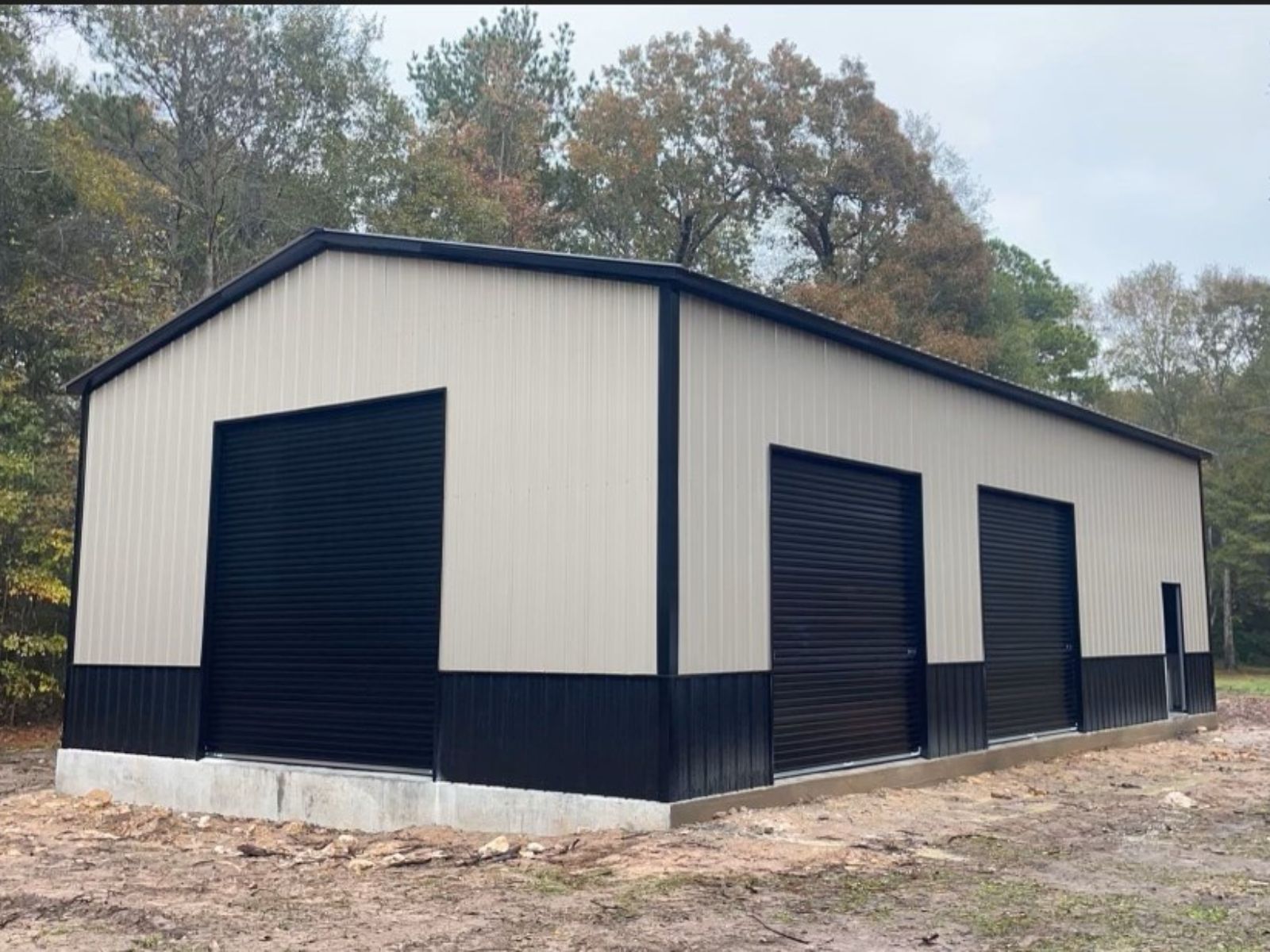 30'x50'x14' Beige and Navy Blue Commercial Steel Garage with three navy blue roll up doors and one walk in door.