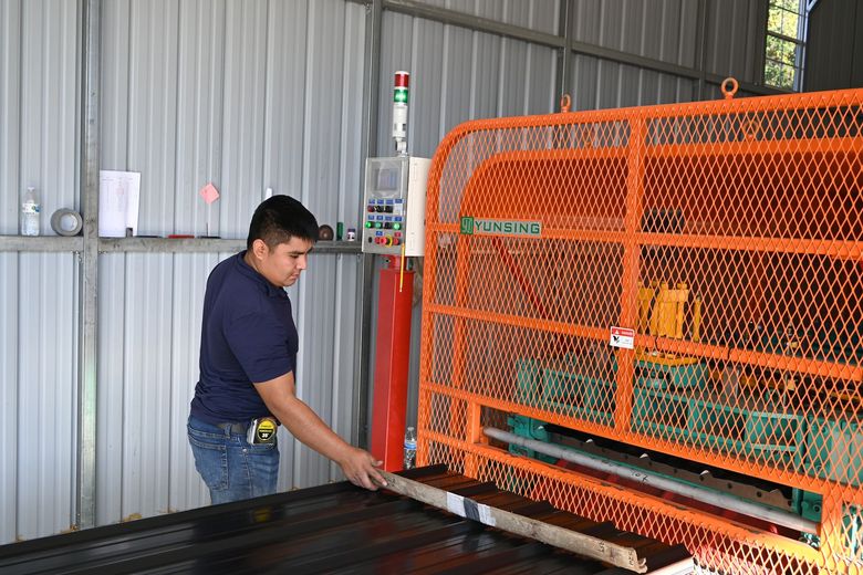 A worker guides a piece of black sheet metal to be cut at the East Texas Carport manufacturing facility in Longview, TX.