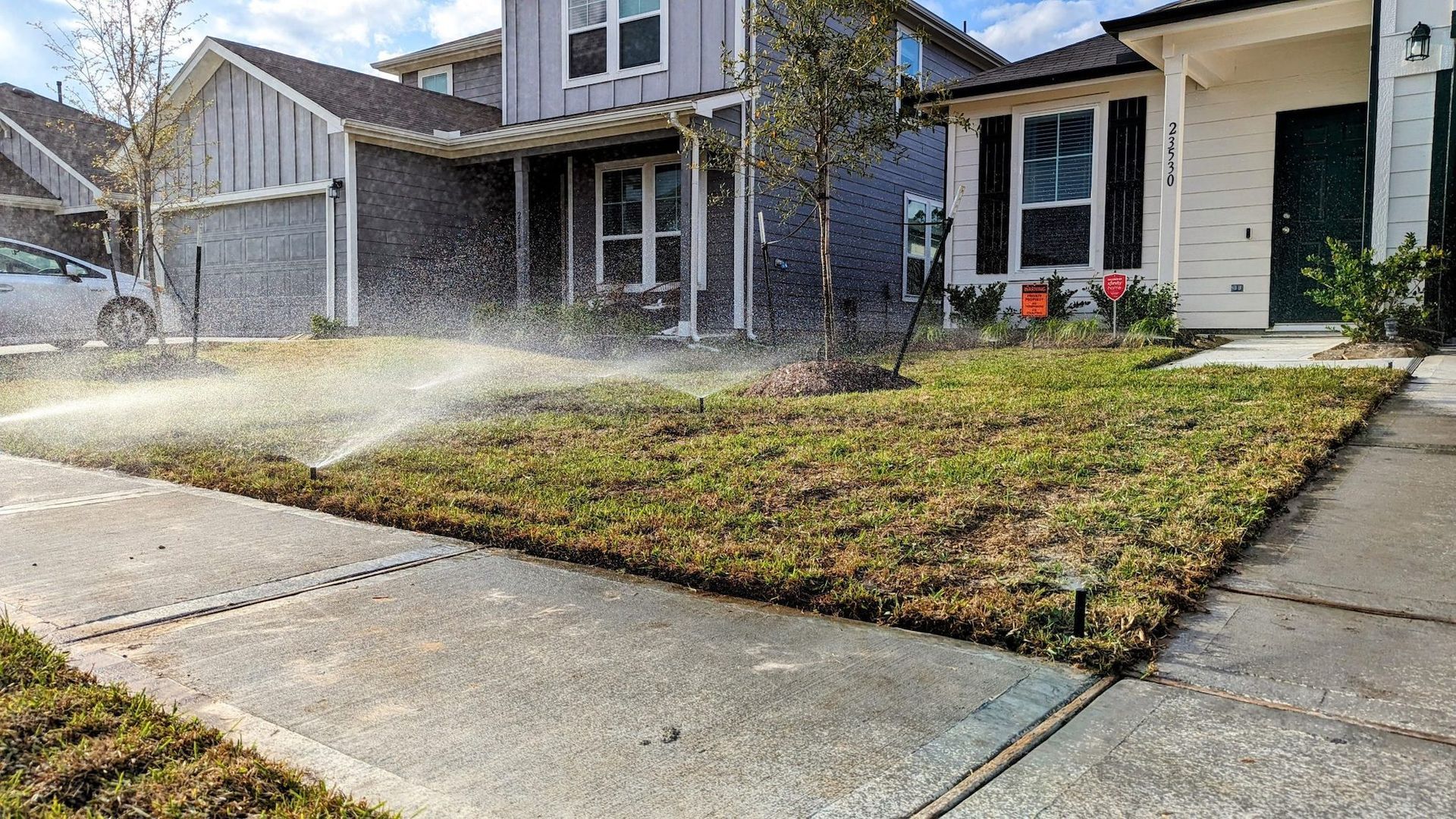 A lawn sprinkler is spraying water on a lush green lawn in front of a house.