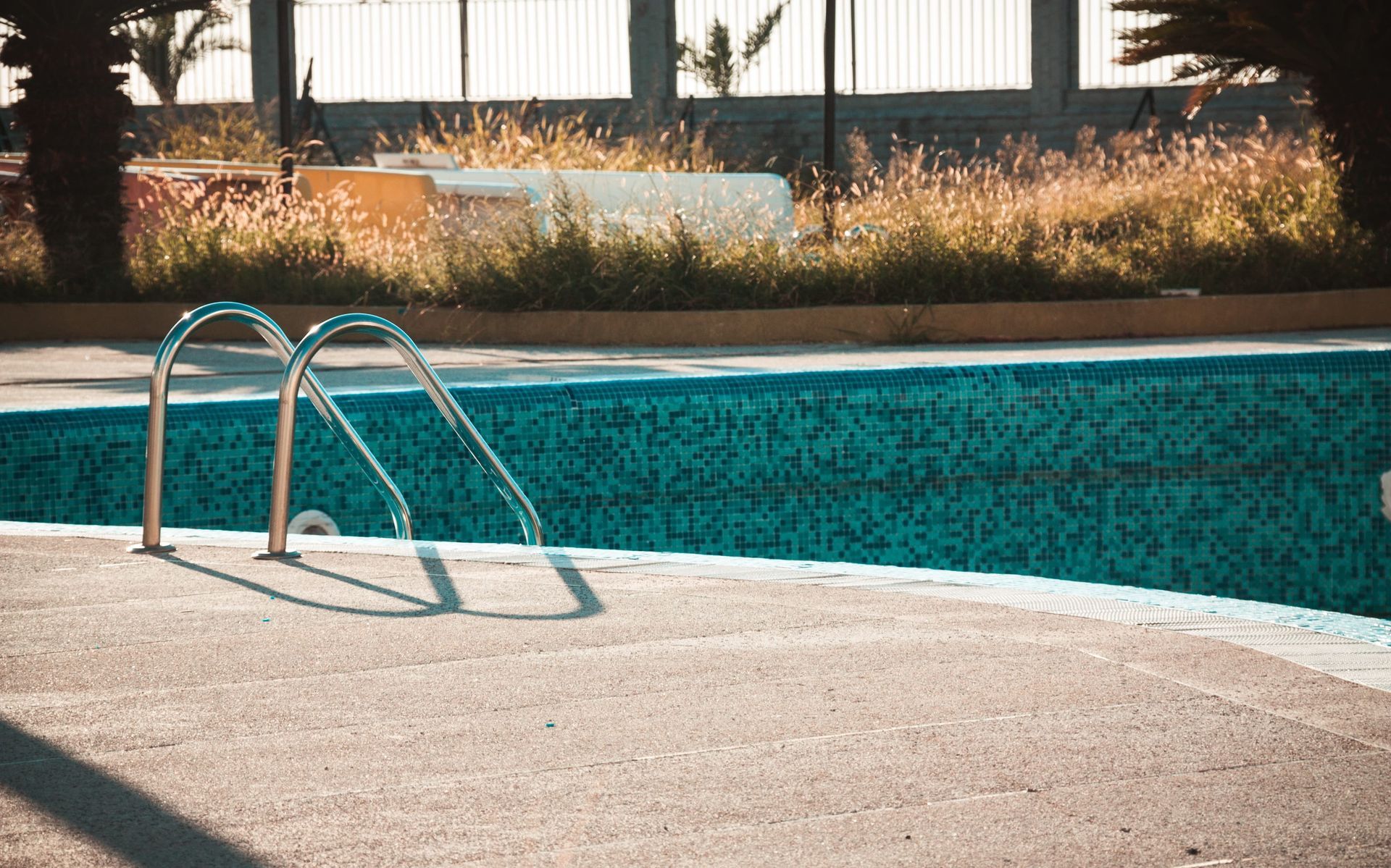 Swimming pool ladder by the edge of a turquoise pool with concrete deck and grassy background