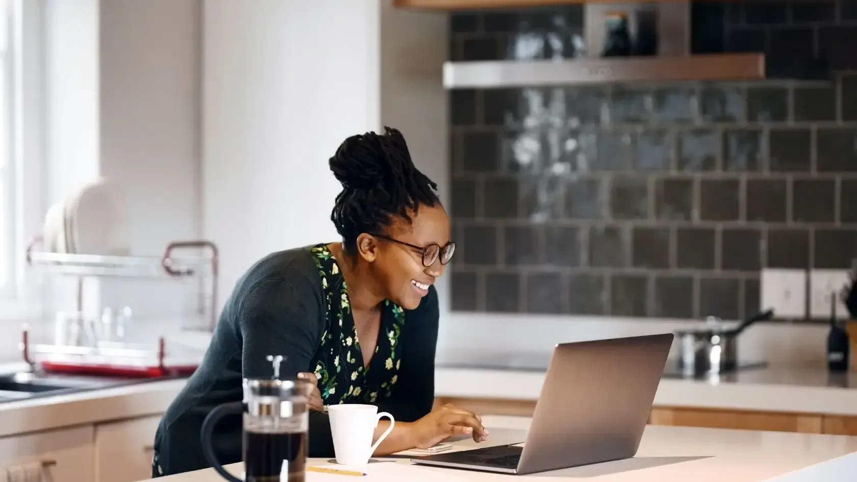 A woman is sitting at a kitchen counter using a laptop computer.