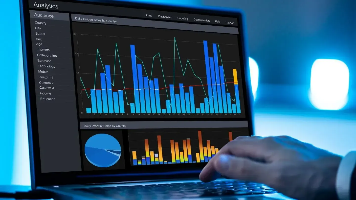 Person using a laptop displaying data visualizations with blue and orange bar graphs and a pie chart.