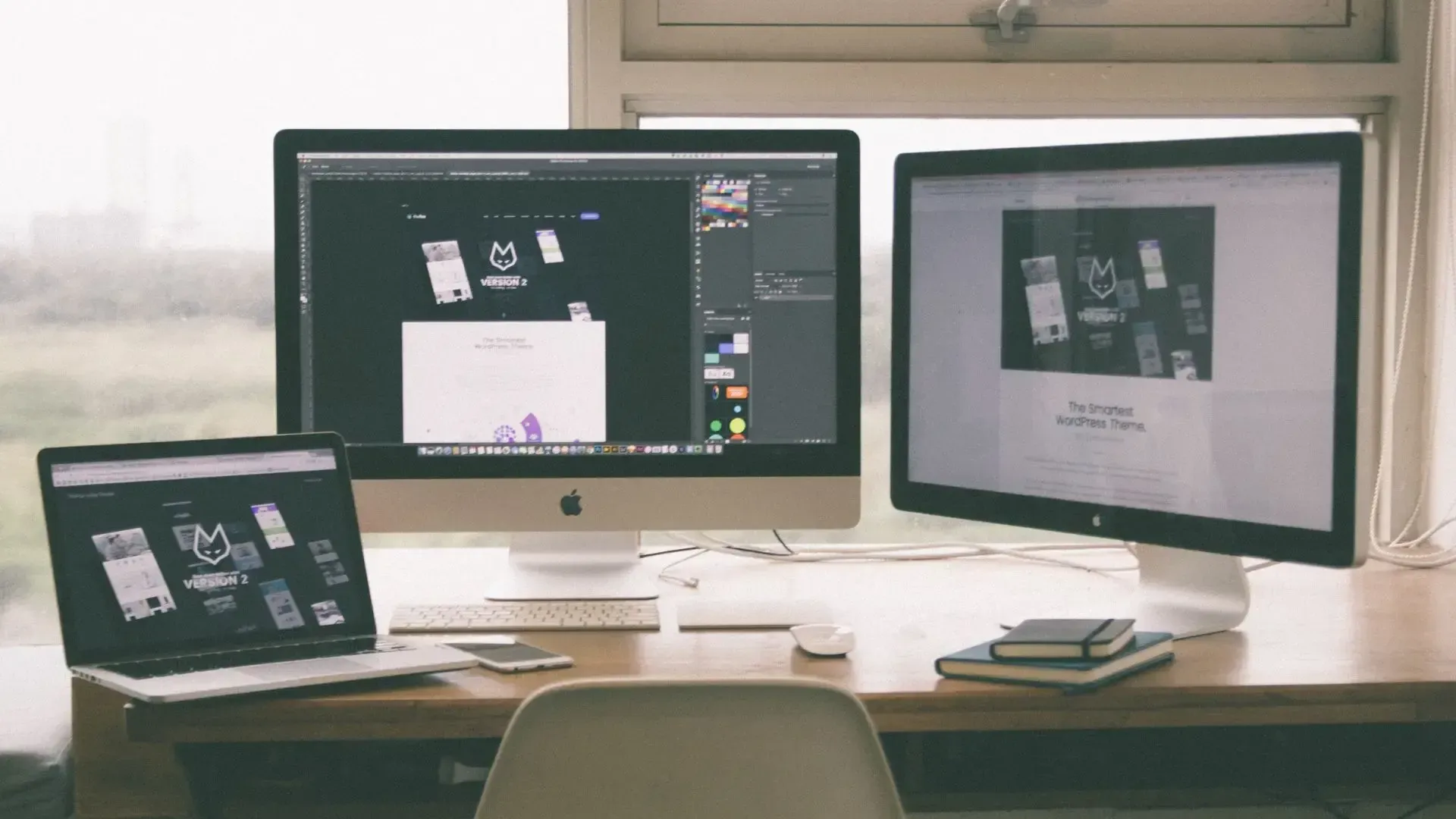 Desk with three computer monitors and a laptop displaying design work.