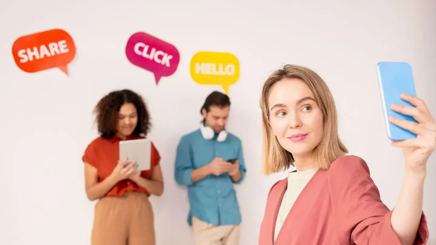Woman taking a selfie with phone. Two people use tablets/phones in the background. Speech bubbles with words.