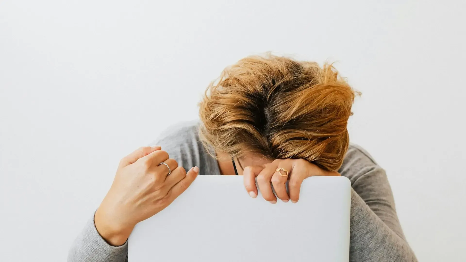 Woman with head resting on a laptop, showing frustration or stress.