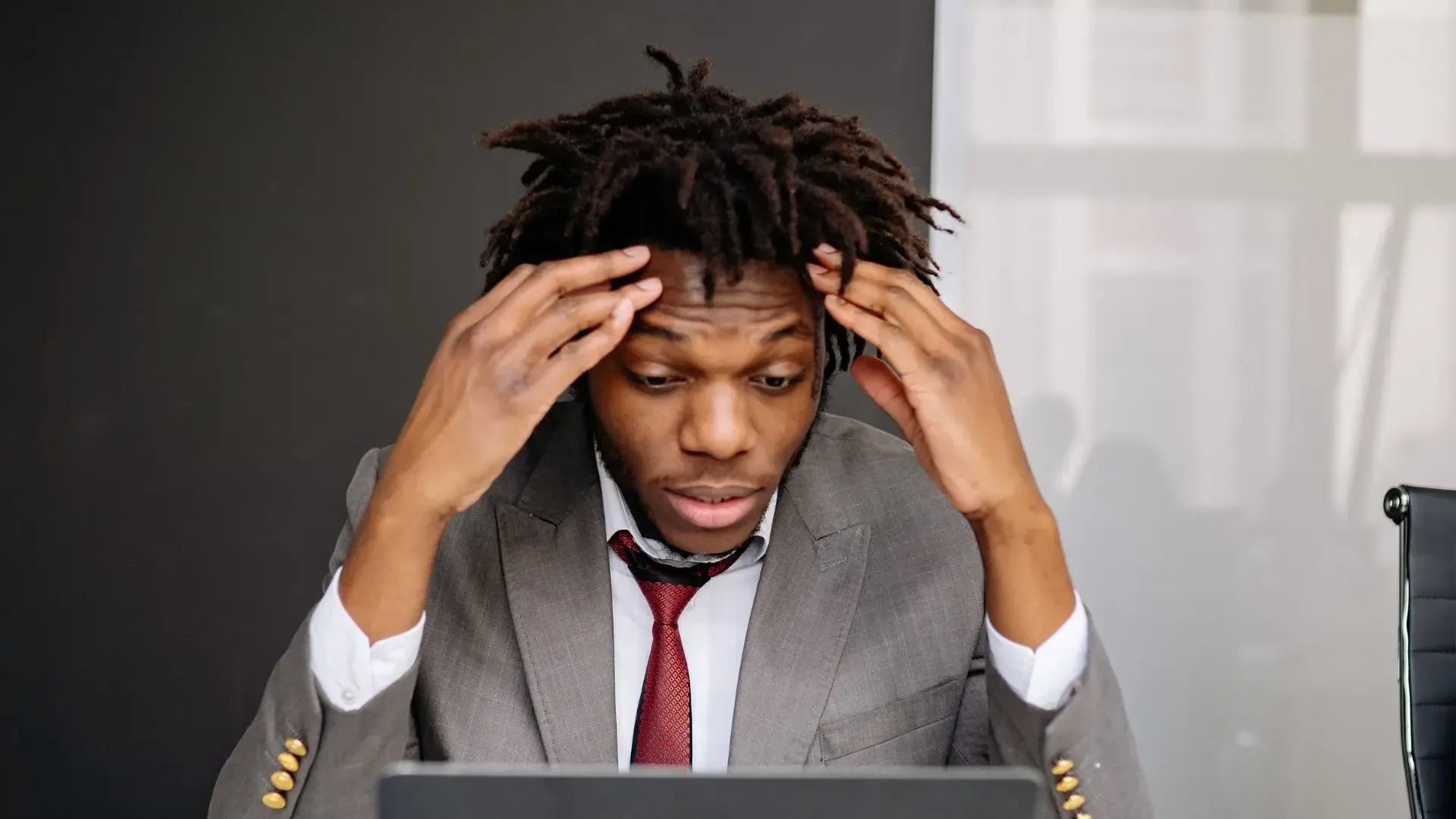 Man in suit, hands on head, looking at a laptop with a distressed expression.