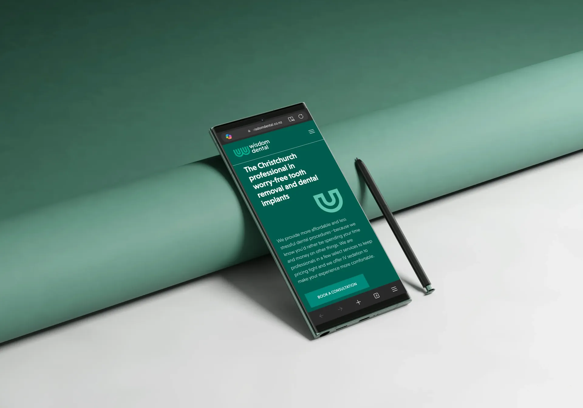 Smartphone displaying text on a green screen, propped against a cylinder on a green surface. A stylus leans against the phone.