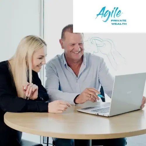 A man and a woman are sitting at a table looking at a laptop