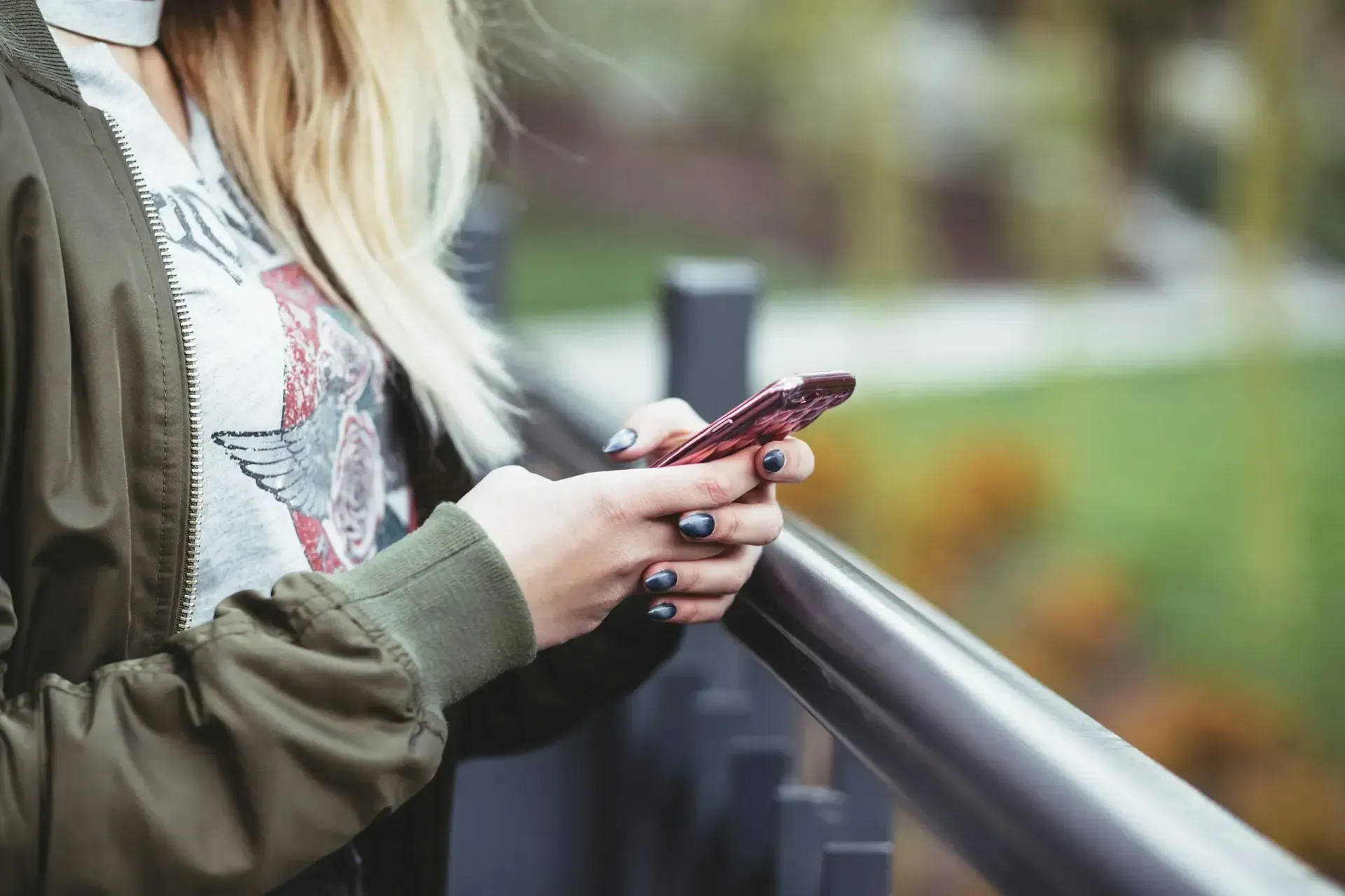 A woman is standing on a bridge looking at her cell phone.