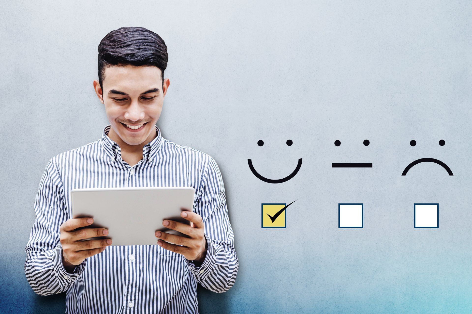 a man is holding a tablet in front of a wall with smiley faces on it .