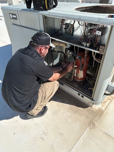 HVAC technician kneeling to work on a rooftop air conditioning unit.