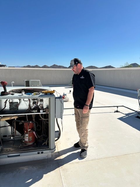 Man in work clothes inspecting an air conditioning unit on a rooftop. Bright, sunny day.
