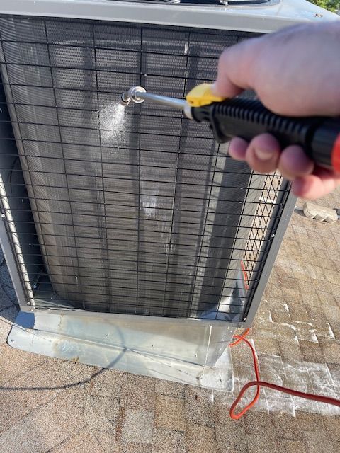 Person spraying an outdoor AC unit with a cleaning product.