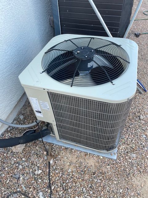 Air conditioning unit outside a building, with fan and metal grill visible.