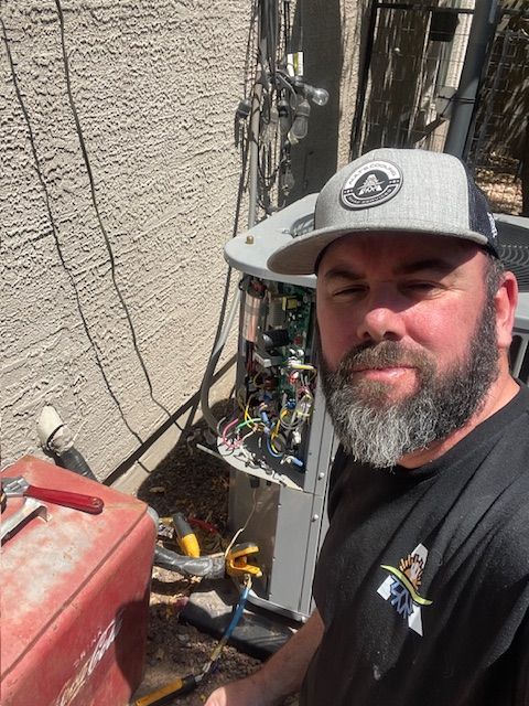 A man with a beard and a cap working on an AC unit outdoors.