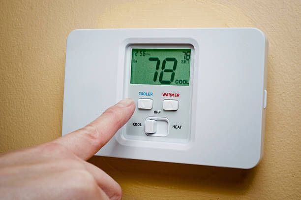 White thermostat on a pale pink wall; displays temperature on its screen.