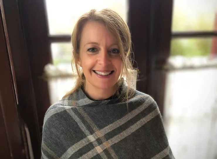 A woman wearing a plaid blanket is smiling for the camera.