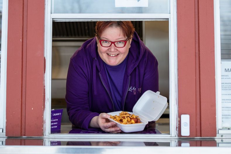 Nainen violetissa takissa pitelee käsissään makkaraperunoita.