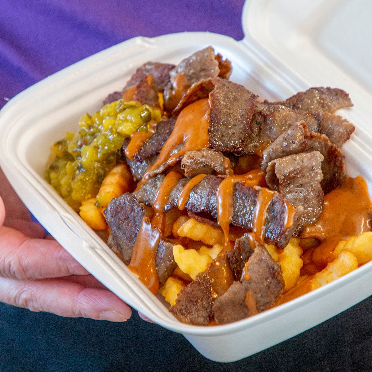 Henkilö pitää kädessään styroksisäiliötä, joka on täytetty lihalla ja ranskalaisilla