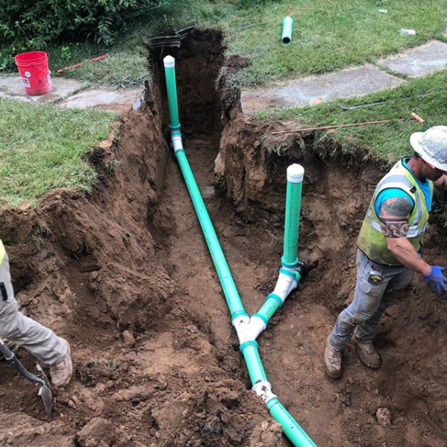 Men are digging a hole in the ground to install green pipes