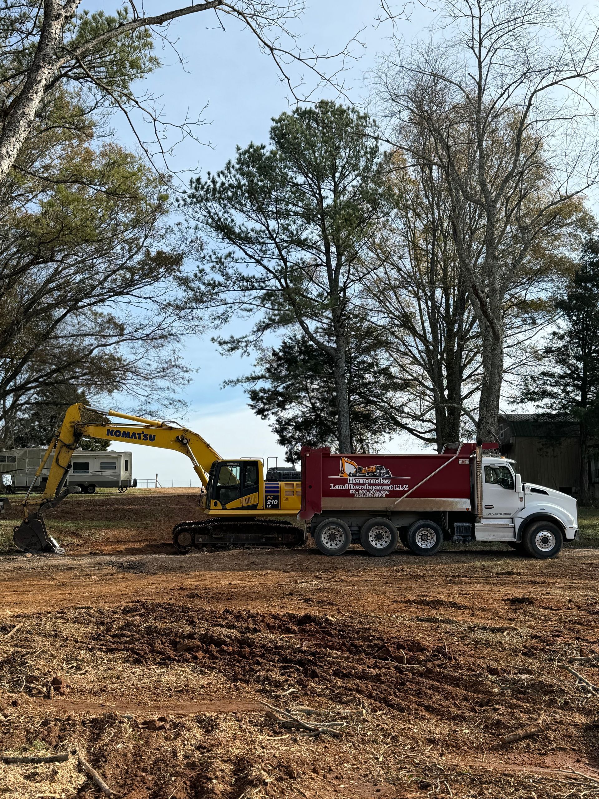 A dump truck and an excavator are parked in a dirt field.