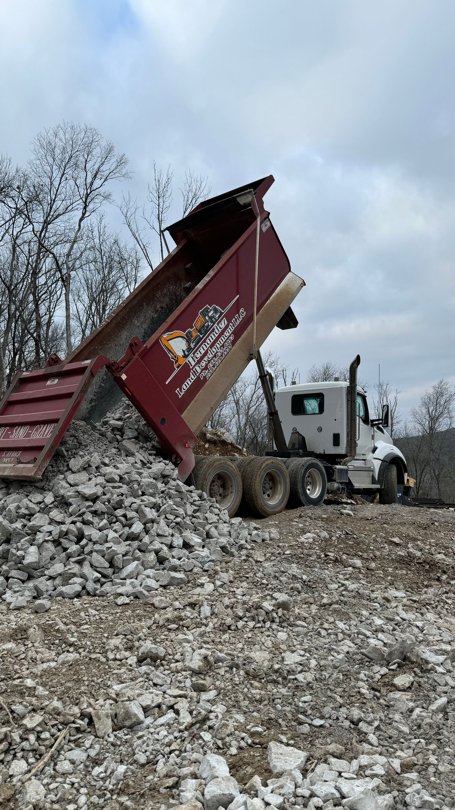 A dump truck is dumping rocks into a pile of rocks.